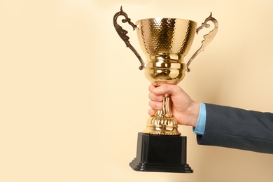 Photo of Man holding golden trophy cup on color background, closeup. Space for text