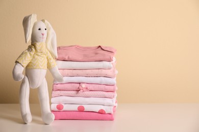 Photo of Stack of baby girl's clothes and toy bunny on white table. Space for text