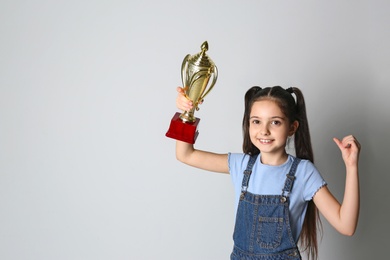 Happy girl with golden winning cup on light background. Space for text