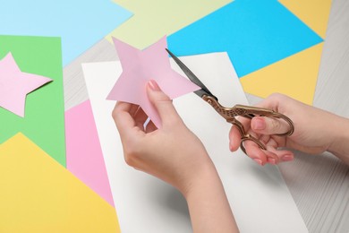 Photo of Woman cutting paper star with scissors at white wooden table, closeup