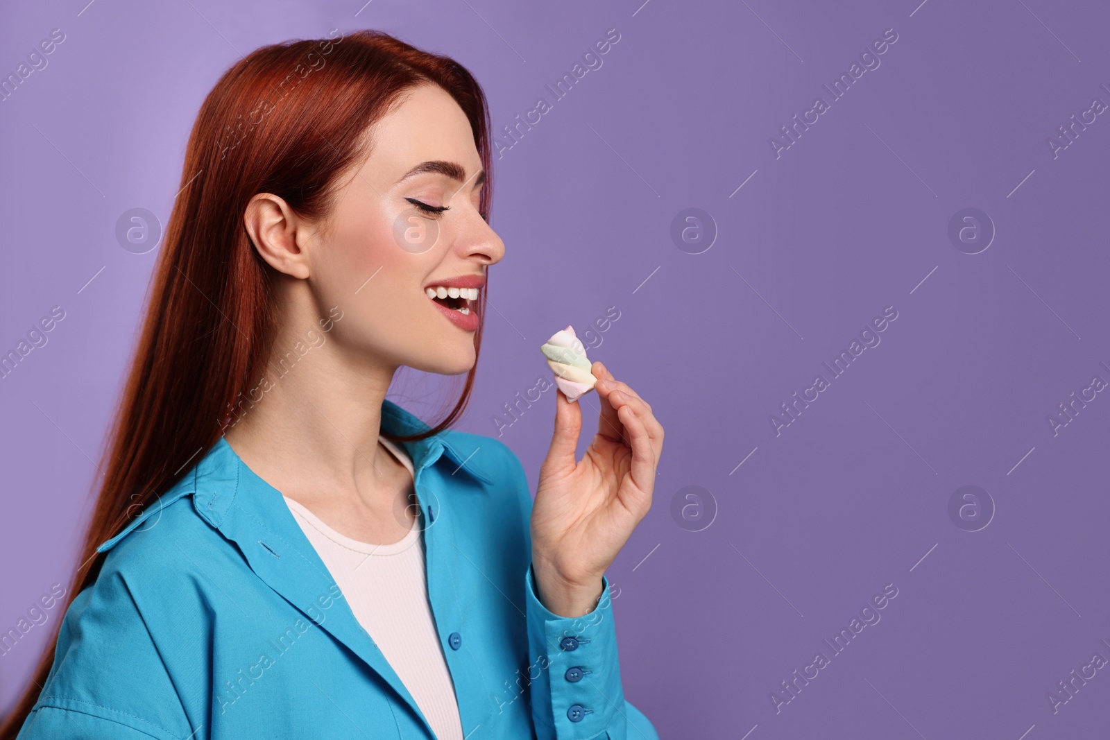 Photo of Happy woman with red dyed hair and marshmallow on purple background, space for text