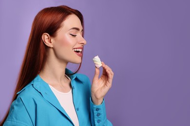 Happy woman with red dyed hair and marshmallow on purple background, space for text