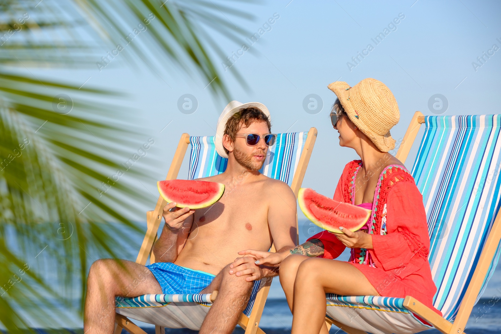 Photo of Young couple with watermelon slices in beach chairs at seacoast