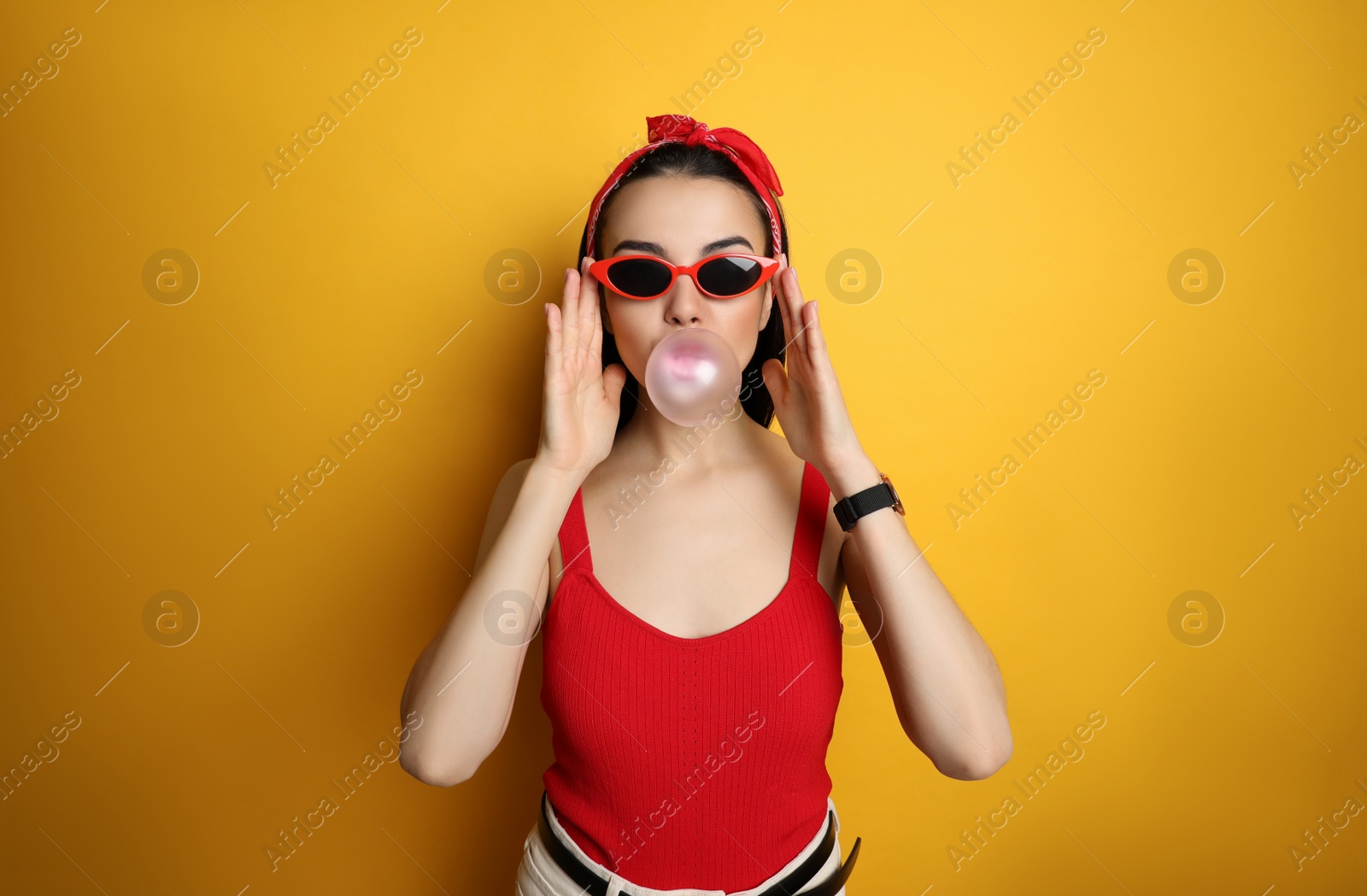 Photo of Fashionable young woman in pin up outfit blowing bubblegum on yellow background