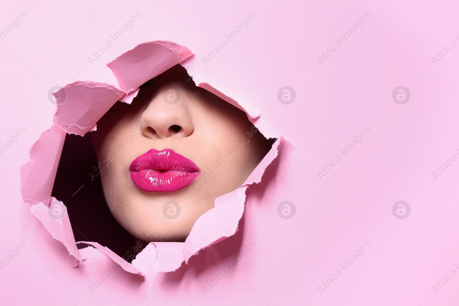 Photo of View of beautiful young woman with perfect lips makeup through hole in color paper. Space for text