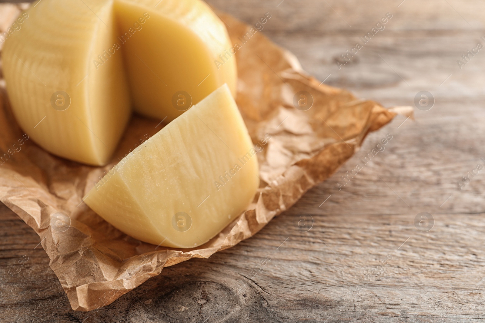 Photo of Parchment paper with cut wheel of delicious cheese on wooden table. Space for text