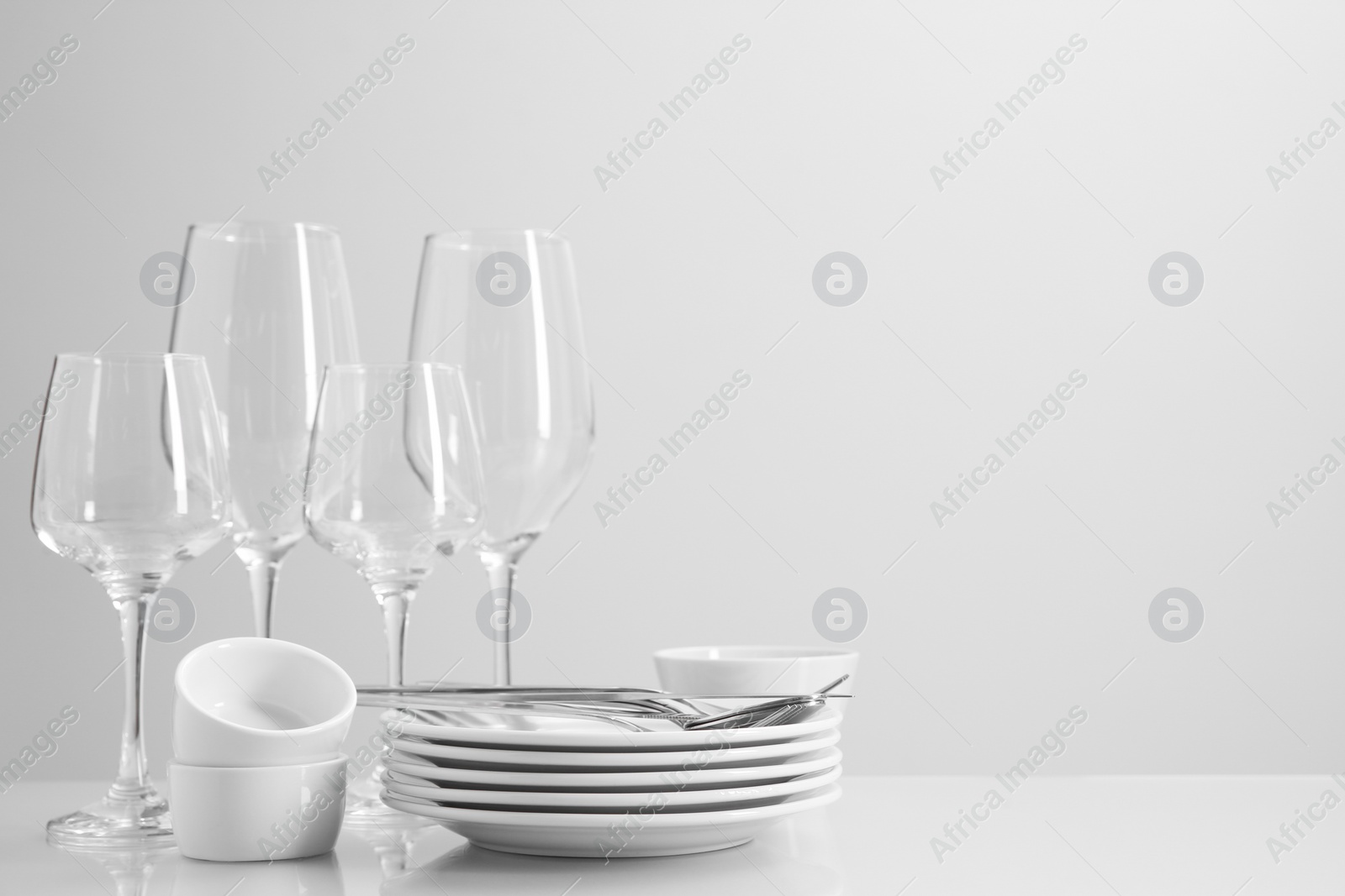 Photo of Set of many clean dishware, cutlery and glasses on light table. Space for text