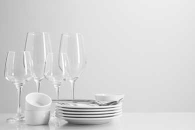 Photo of Set of many clean dishware, cutlery and glasses on light table. Space for text