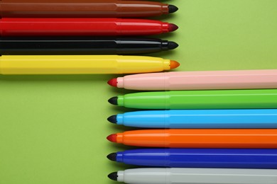 Many different colorful markers on light green background, flat lay