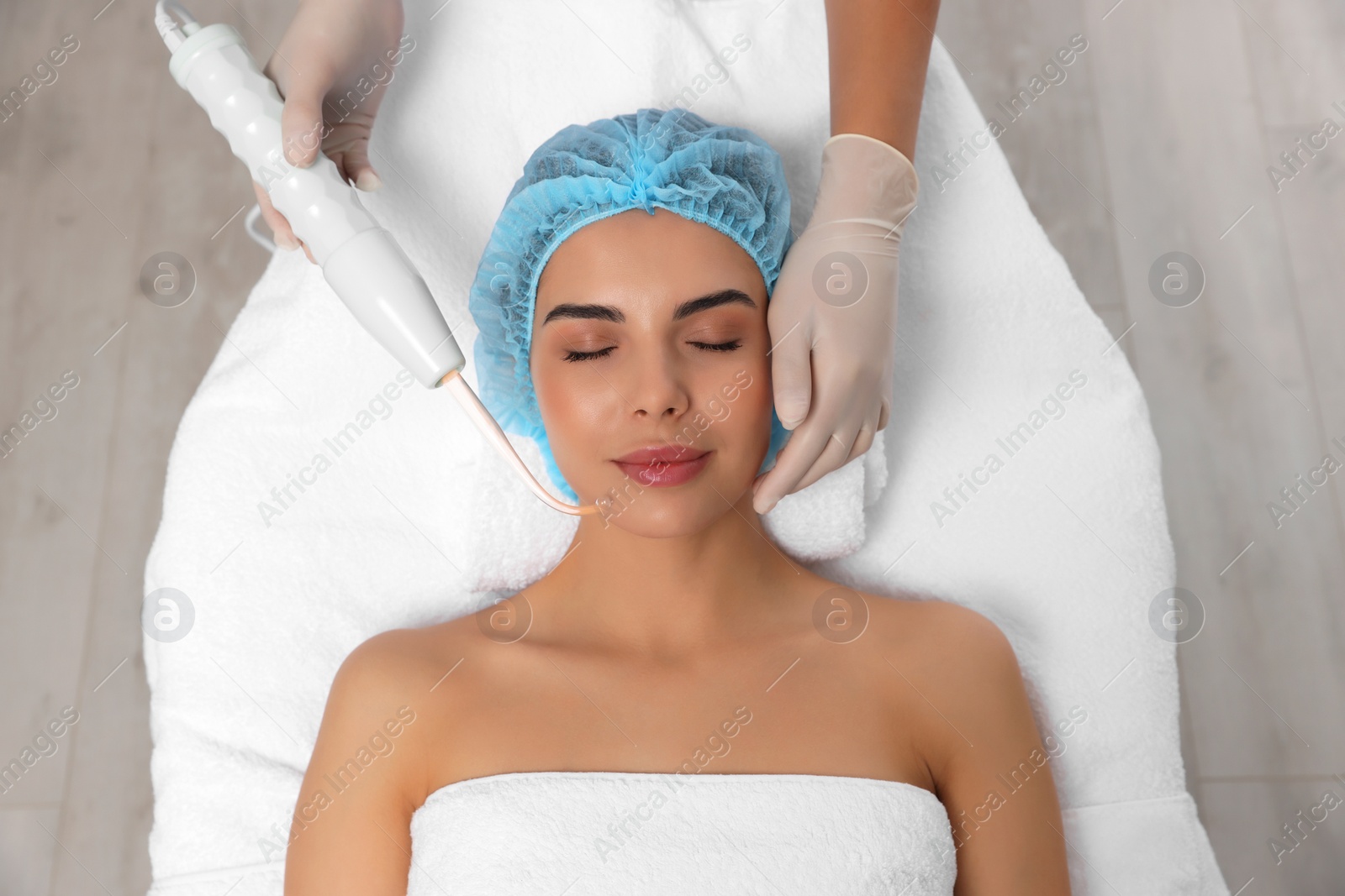 Photo of Young woman undergoing face rejuvenation procedure with darsonval in salon, top view