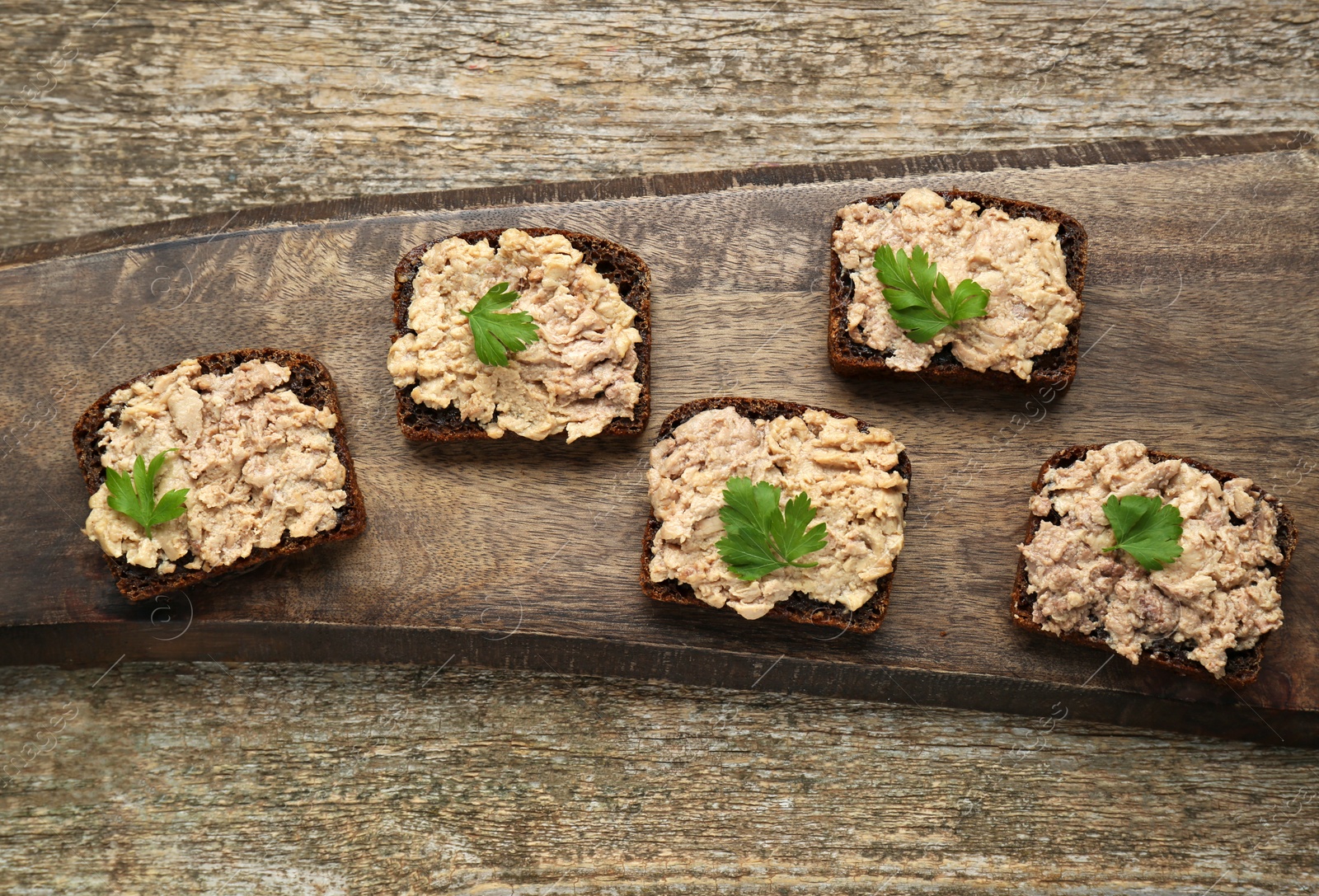 Photo of Tasty sandwiches with cod liver and parsley on wooden table, top view