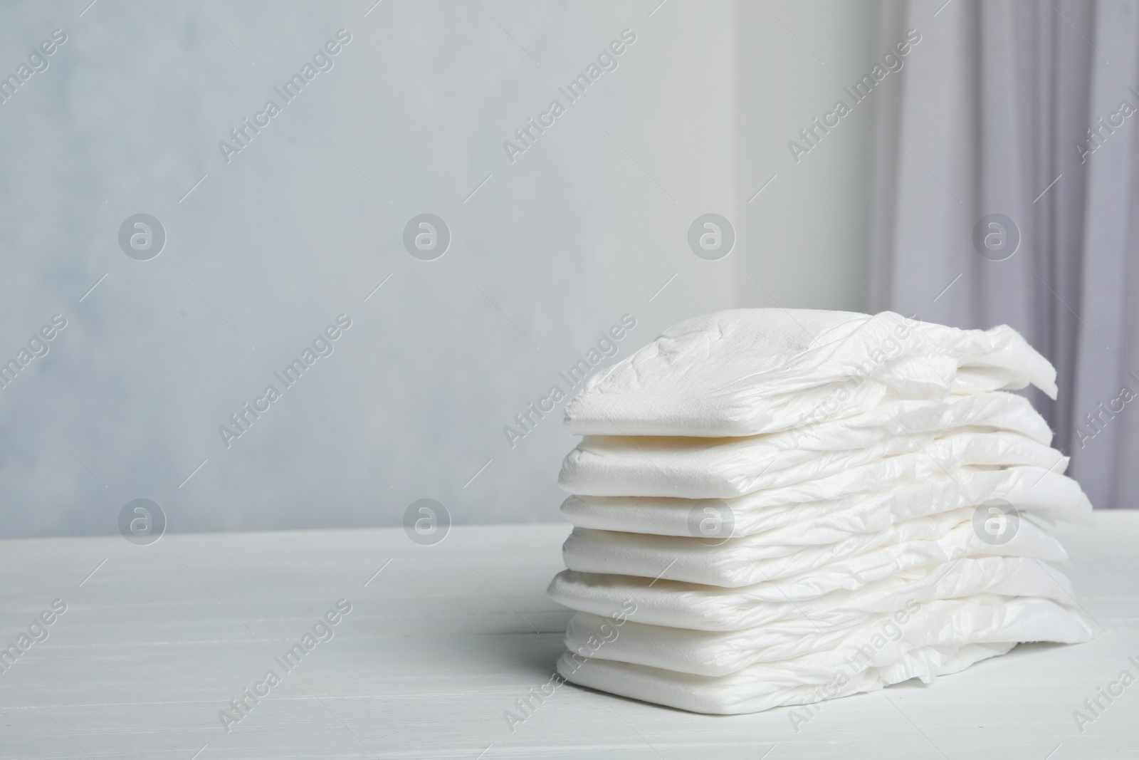 Photo of Stack of baby diapers on white wooden table against grey background. Space for text