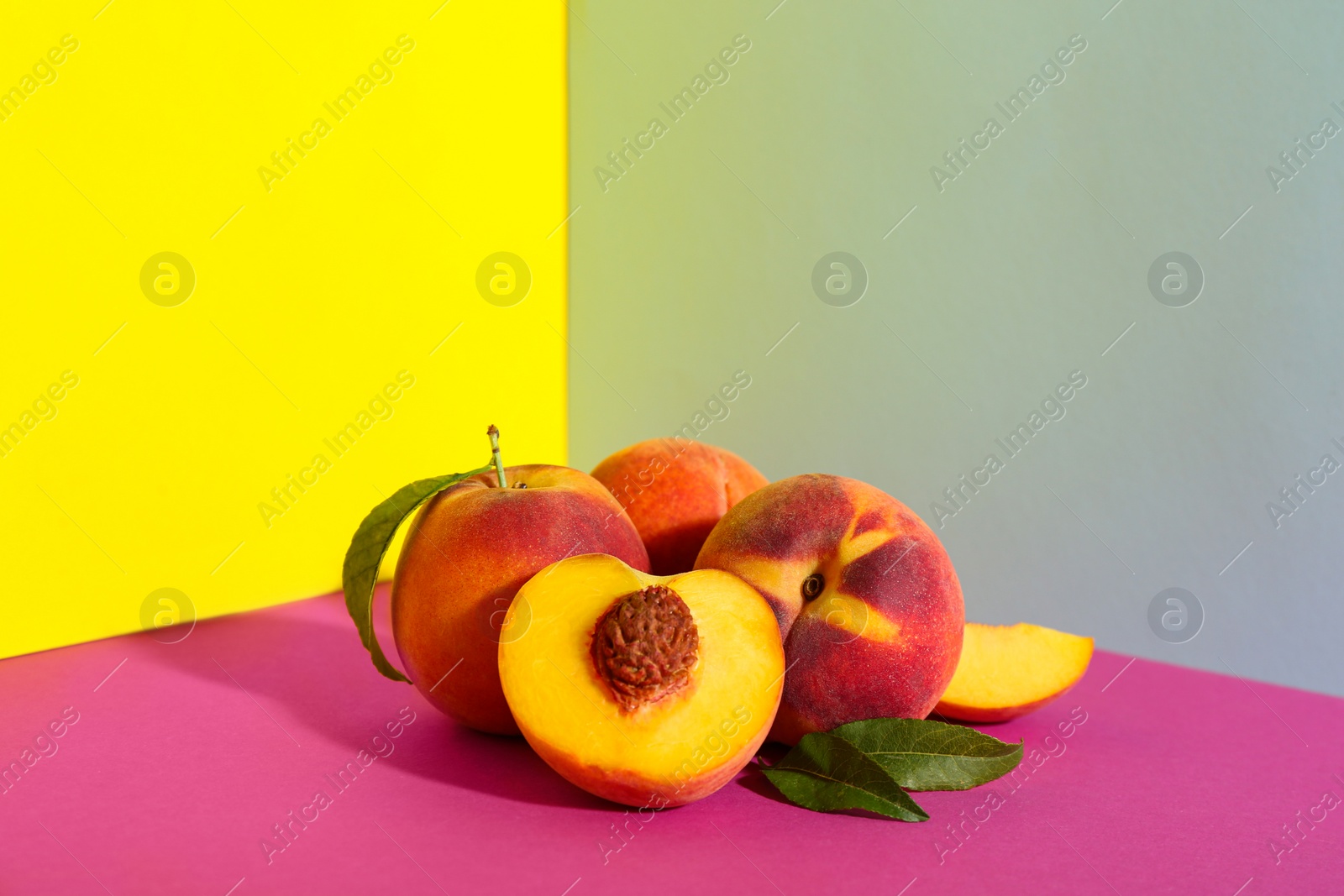 Photo of Fresh ripe peaches and green leaves on color background