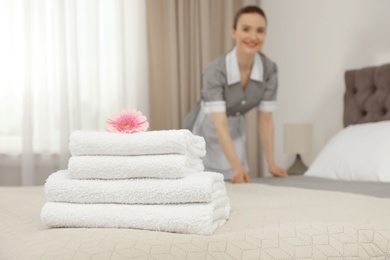 Photo of Stack of clean towels on bed and blurred chambermaid in hotel room, closeup. Space for text