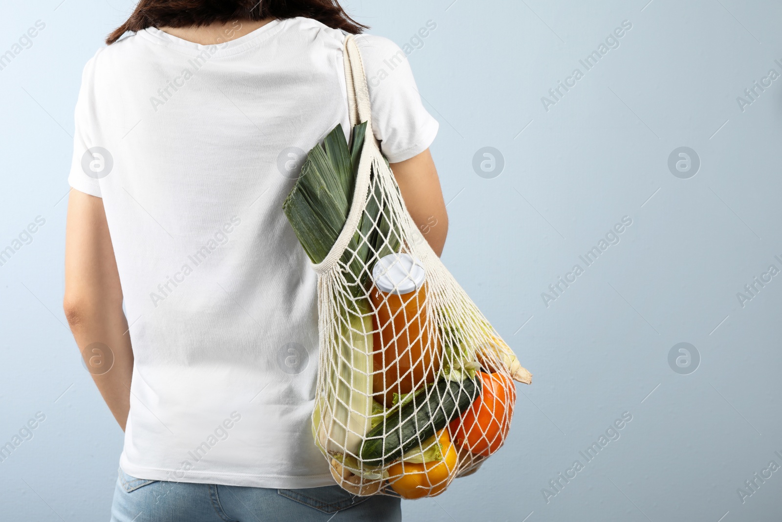 Photo of Woman holding mesh bag with fresh vegetables on grey background, closeup. Space for text