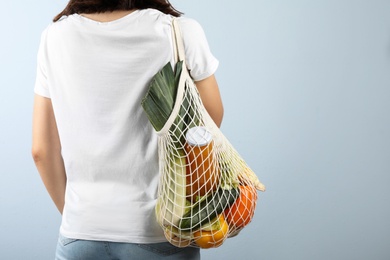 Woman holding mesh bag with fresh vegetables on grey background, closeup. Space for text