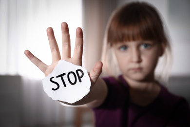 Abused little girl with sign STOP indoors, focus on hand. Domestic violence concept
