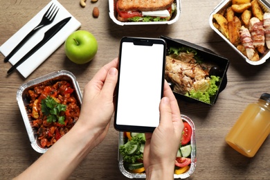 Photo of Top view of woman holding smartphone over wooden table with lunchboxes,  mockup for design. Healthy food delivery