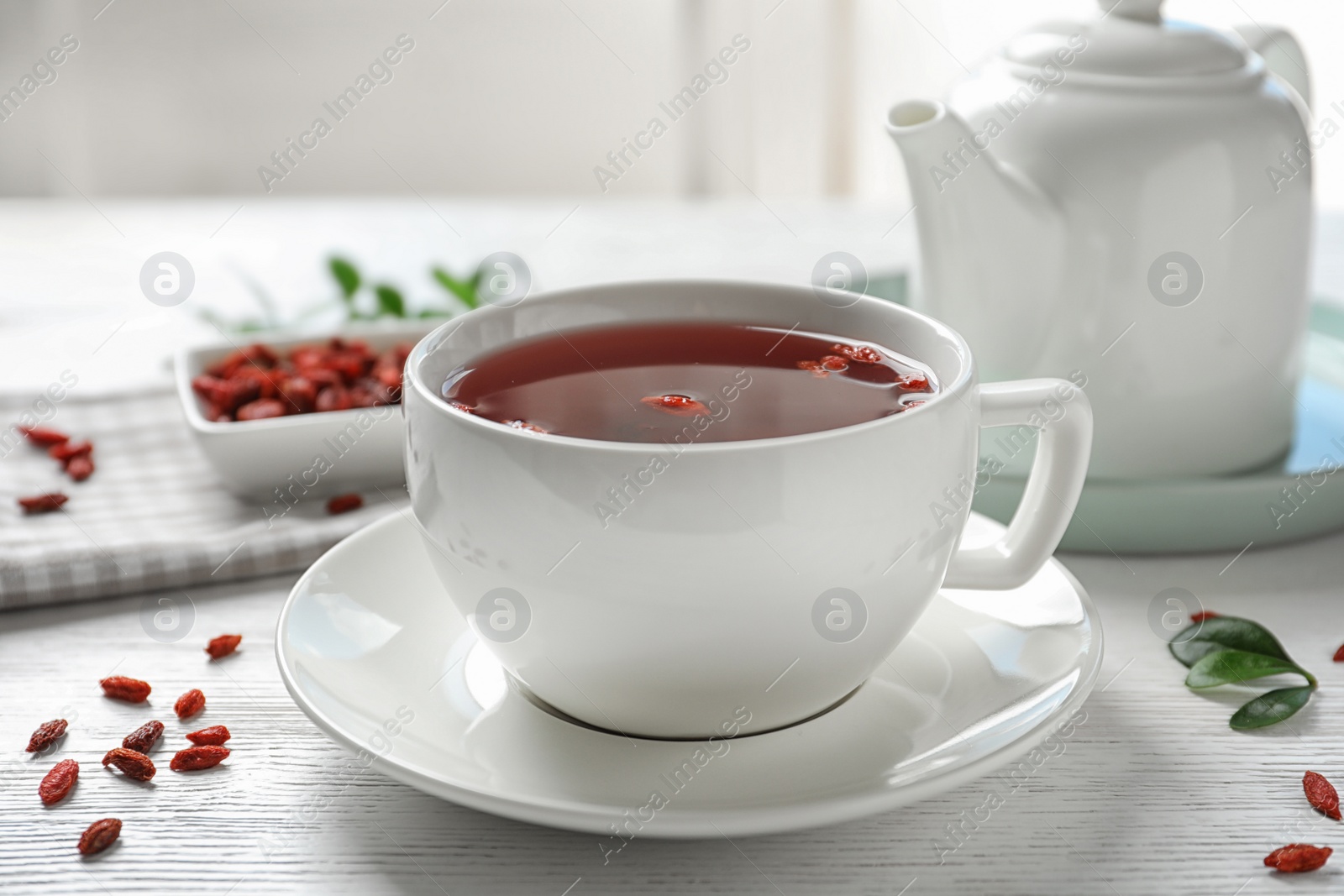 Photo of Healthy goji tea in cup on white wooden table