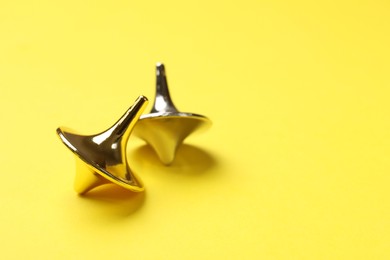 Photo of Golden and silver spinning tops on yellow background, closeup. Space for text