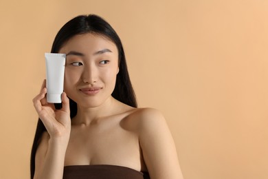 Photo of Beautiful young woman holding sun protection cream on beige background, space for text