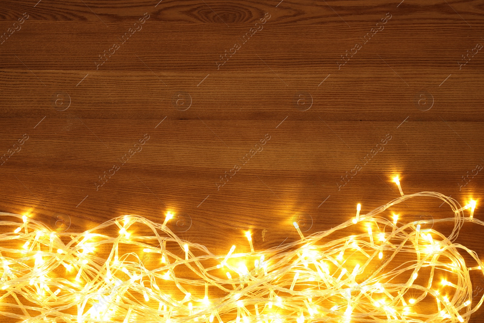 Photo of Beautiful glowing Christmas lights on wooden table, top view. Space for text