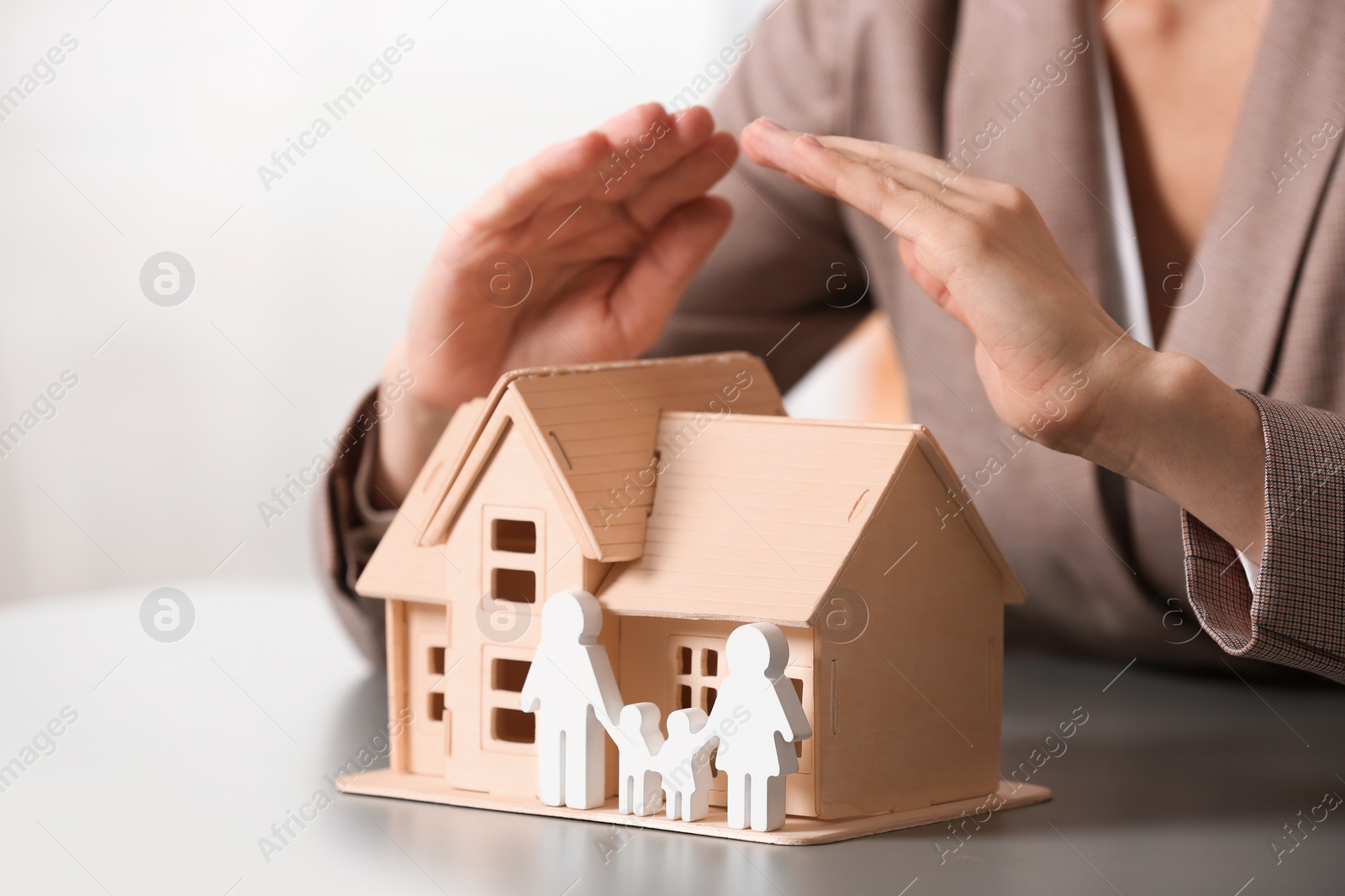 Photo of Female agent covering house model and family at table, closeup. Home insurance