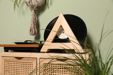 Photo of Vinyl records and player on wooden cabinet near light green wall