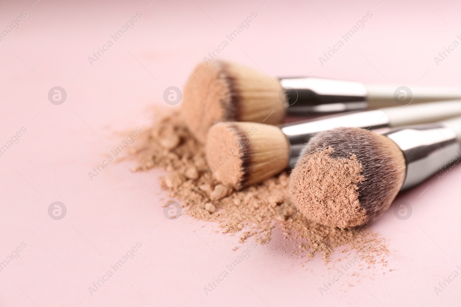 Photo of Different makeup brushes with crushed cosmetic product on pink background, closeup. Space for text