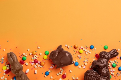 Photo of Flat lay composition with chocolate Easter bunnies and candies on orange background. Space for text
