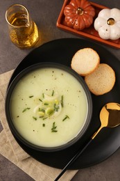 Bowl of tasty leek soup, spoon and bread on grey table, flat lay