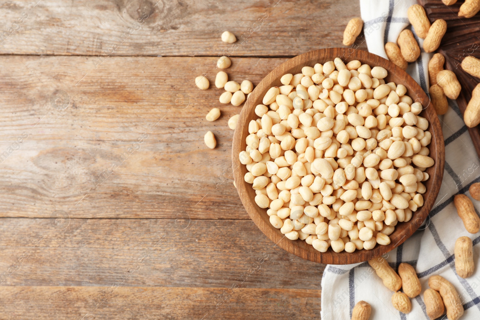 Photo of Shelled peanuts in bowl, napkin and space for text on wooden table, top view