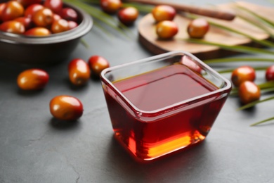 Photo of Palm oil in glass bowl, tropical leaf and fruits on black table