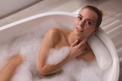 Photo of Beautiful woman taking bath in tub with foam indoors, top view