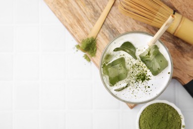 Photo of Glass of tasty iced matcha latte, bamboo whisk and powder on white tiled table, flat lay. Space for text