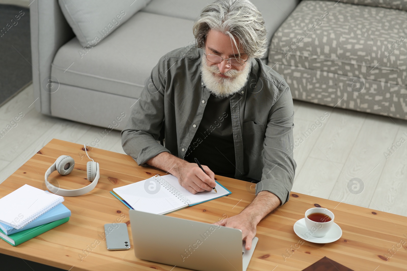 Photo of Middle aged man with laptop and notebook learning at table indoors