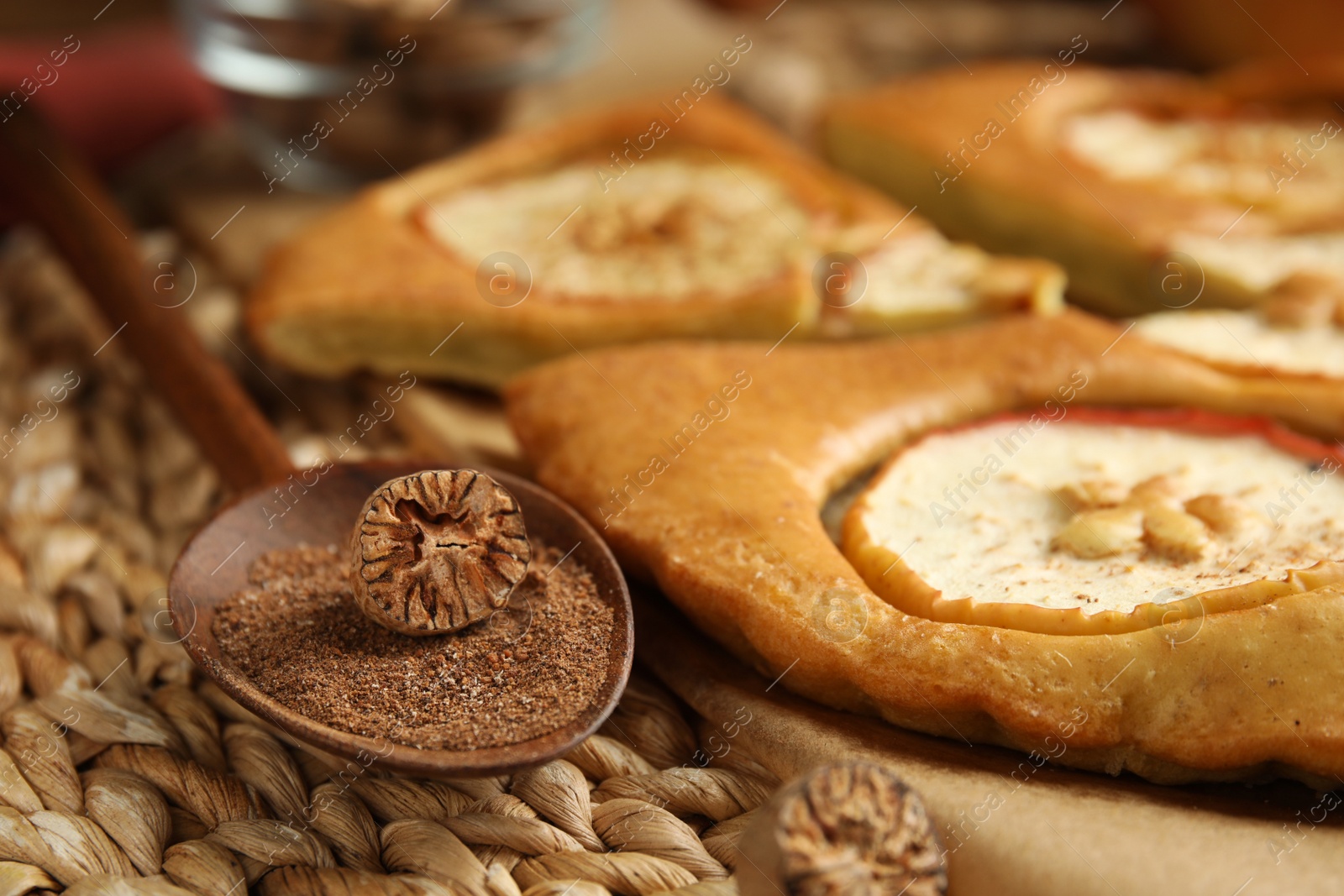 Photo of Nutmeg powder, seed and tasty apple pie on wicker mat, closeup