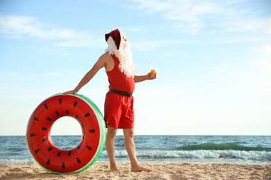 Photo of Santa Claus with cocktail and inflatable ring on beach, space for text. Christmas vacation