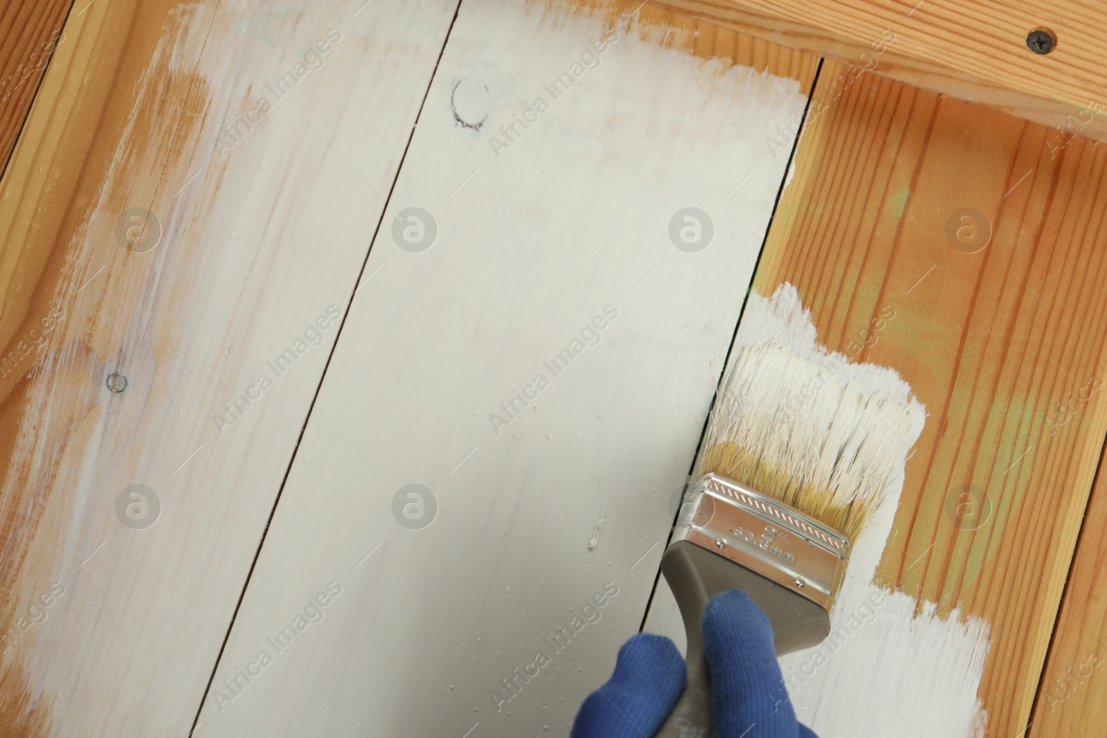 Photo of Worker applying white paint onto wooden surface, above view. Space for text