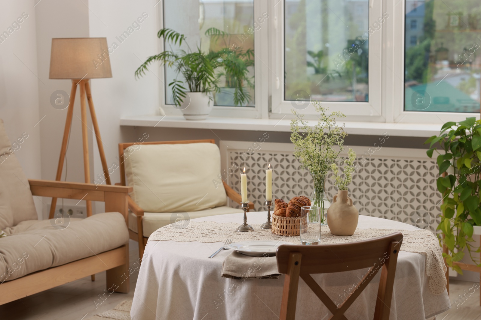 Photo of Clean dishware, flowers, fresh pastries and burning candles on table in stylish dining room