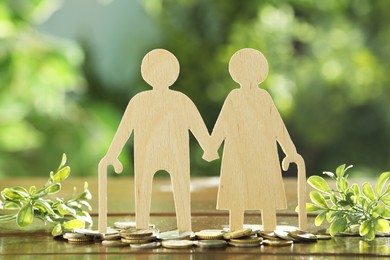 Photo of Pension savings. Figure of senior couple, coins and green twigs on wooden table outdoors