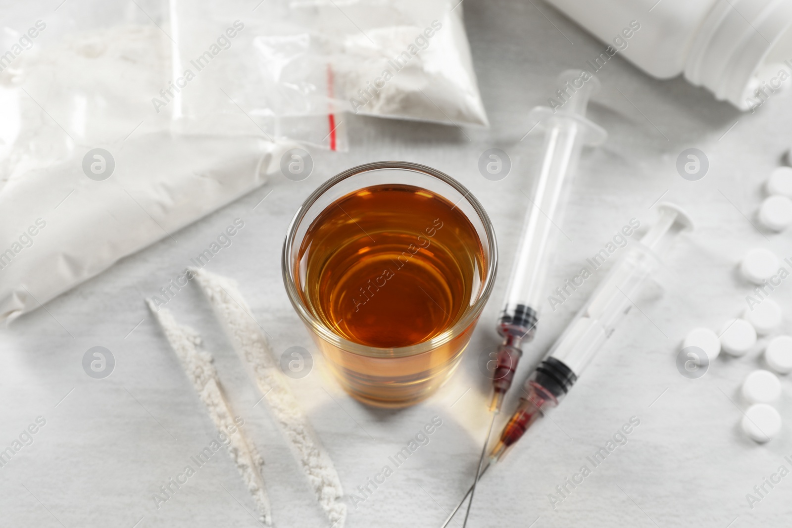 Photo of Alcohol and drug addiction. Whiskey in glass, syringes, cocaine and pills on white table