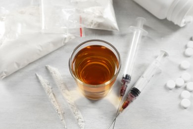 Photo of Alcohol and drug addiction. Whiskey in glass, syringes, cocaine and pills on white table