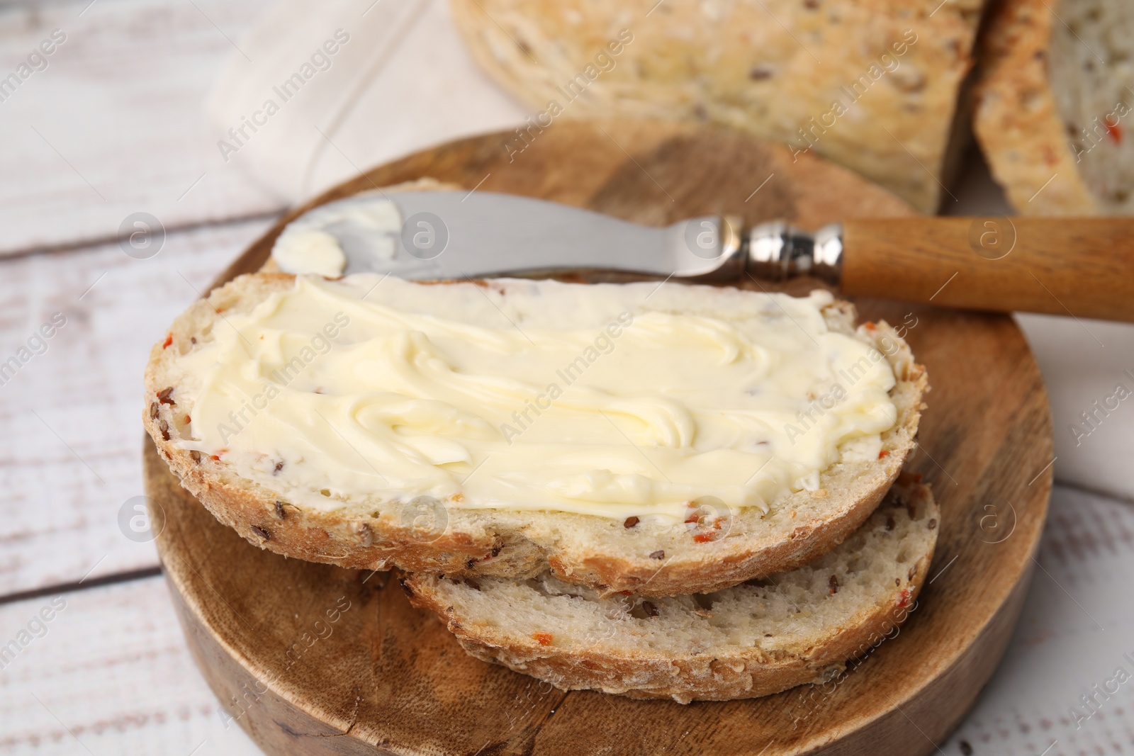 Photo of Slices of tasty bread with butter and knife on white wooden table, closeup