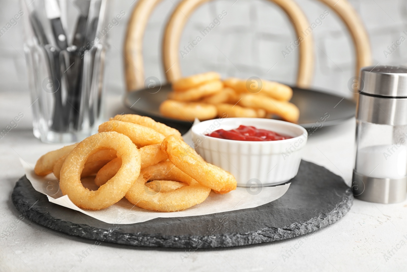 Photo of Slate plate with onion rings and bowl of sauce on table