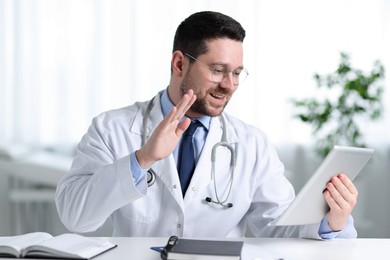 Photo of Smiling doctor having online consultation via tablet at table in clinic