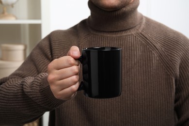 Man holding black mug at home, closeup. Mockup for design