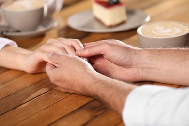 Photo of Romantic date. Couple holding hands together at wooden table in cafe, closeup
