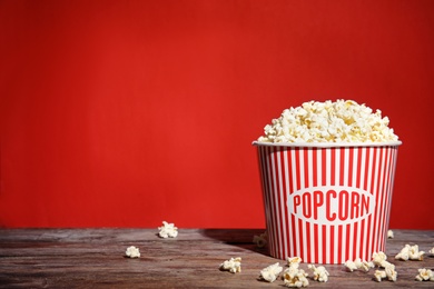 Bucket of tasty popcorn on table against red background, space for text. Watching cinema