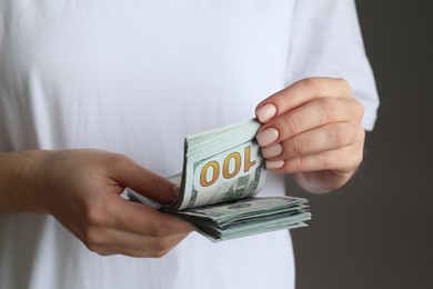 Money exchange. Woman counting dollar banknotes on grey background, closeup